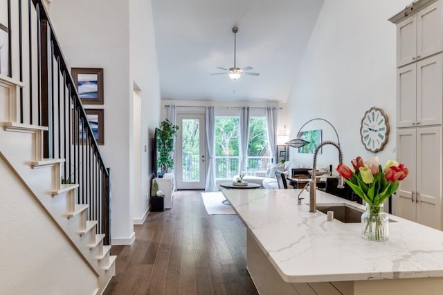 kitchen featuring light stone countertops, a sink, a ceiling fan, open floor plan, and dark wood-type flooring