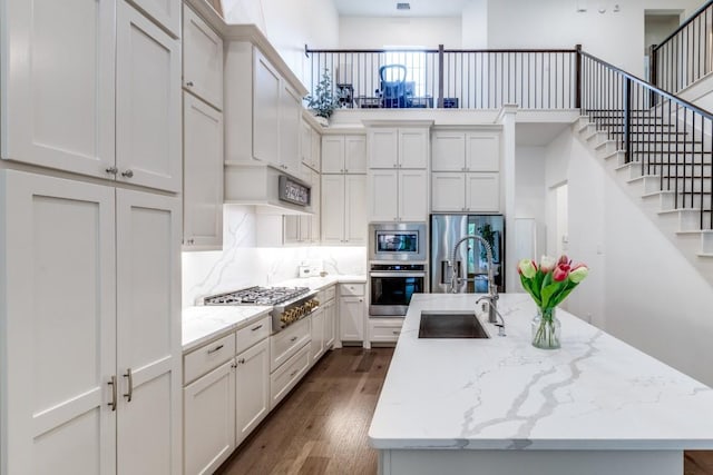 kitchen with appliances with stainless steel finishes, a sink, an island with sink, decorative backsplash, and dark wood-type flooring