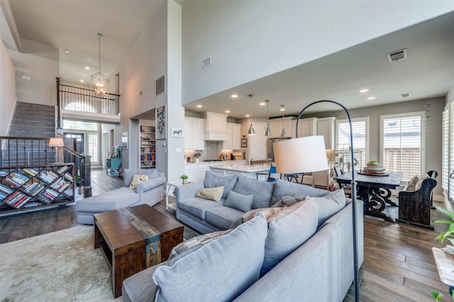 living area with an inviting chandelier, a towering ceiling, dark wood-style floors, and visible vents