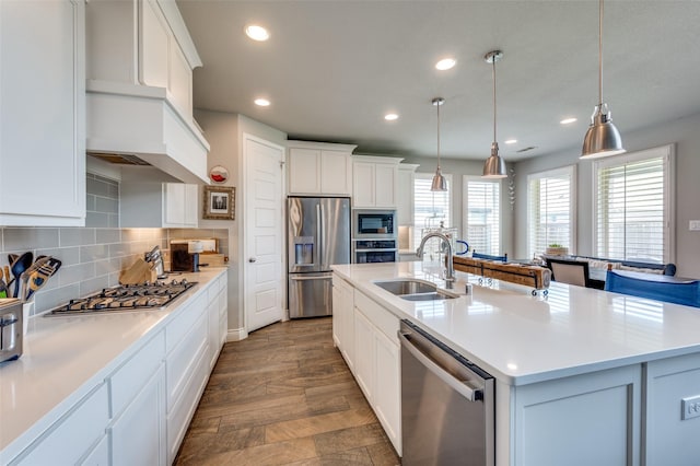 kitchen featuring backsplash, a sink, white cabinets, stainless steel appliances, and an island with sink