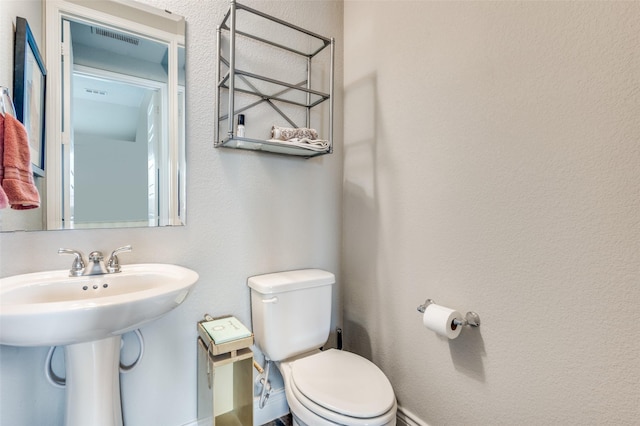 half bath featuring toilet, baseboards, visible vents, and a sink