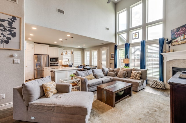 living area with visible vents, a glass covered fireplace, a towering ceiling, and light wood-type flooring