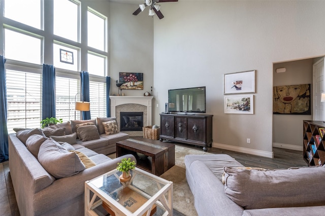 living area featuring ceiling fan, a fireplace, wood finished floors, baseboards, and a high ceiling