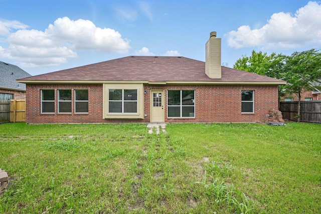 rear view of house with a fenced backyard, a chimney, brick siding, a shingled roof, and a lawn