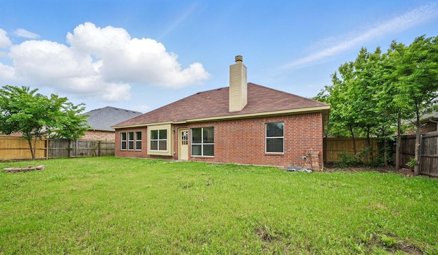 back of house featuring brick siding, a fenced backyard, a yard, and a chimney