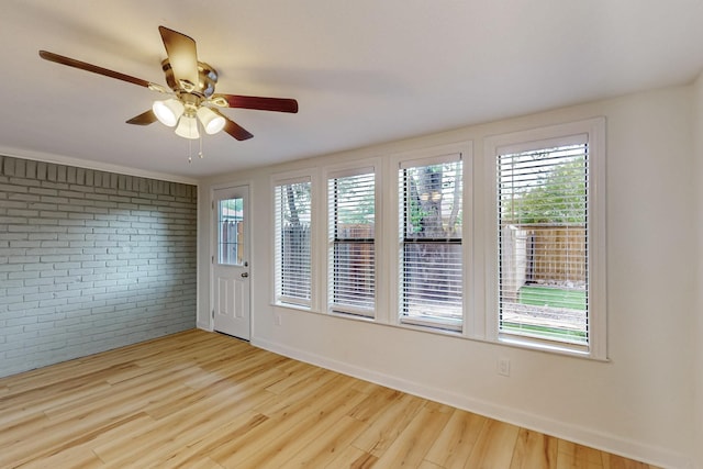 unfurnished room with plenty of natural light, a ceiling fan, brick wall, and wood finished floors