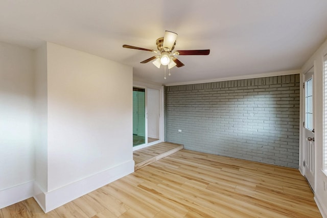 unfurnished room featuring light wood-type flooring, a ceiling fan, baseboards, and brick wall