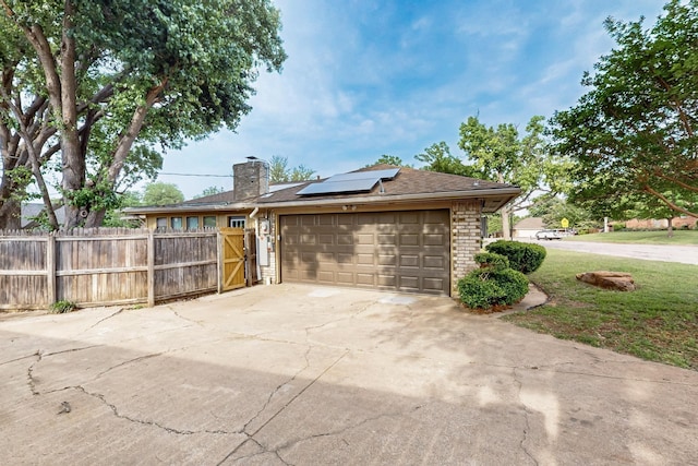 view of home's exterior with driveway, a chimney, brick siding, roof mounted solar panels, and an attached garage