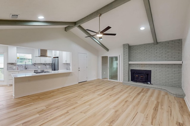 unfurnished living room with vaulted ceiling with beams, light wood-style flooring, ceiling fan, and visible vents