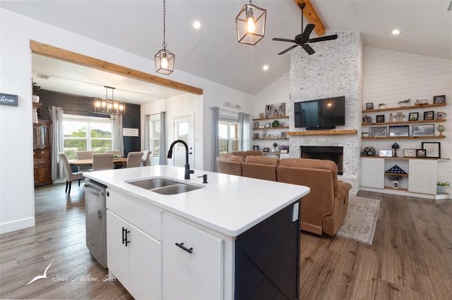 kitchen with a stone fireplace, a center island with sink, wood finished floors, a sink, and beamed ceiling