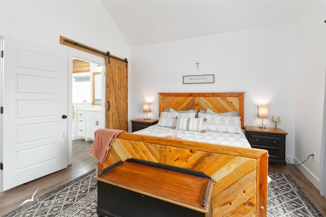 bedroom featuring wood finished floors, ensuite bath, a barn door, and lofted ceiling