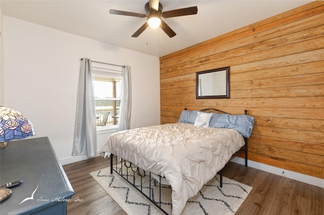 bedroom with wooden walls, a ceiling fan, baseboards, and wood finished floors