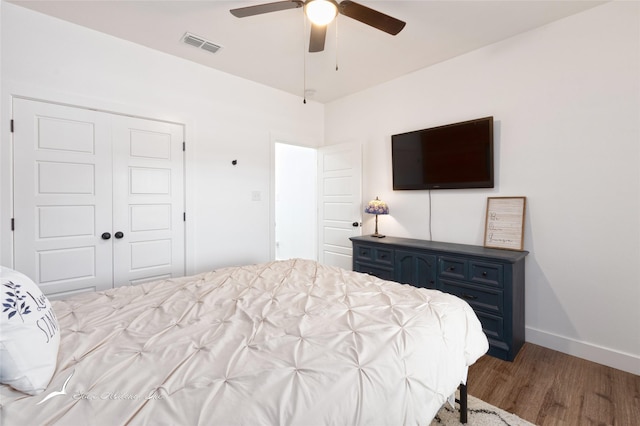 bedroom featuring a ceiling fan, visible vents, wood finished floors, baseboards, and a closet