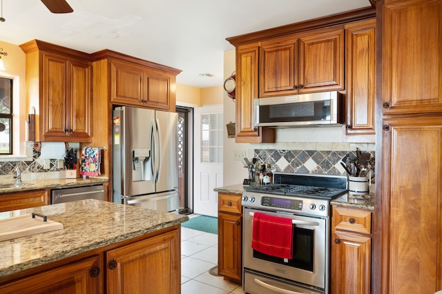 kitchen with appliances with stainless steel finishes, tasteful backsplash, brown cabinetry, and light stone counters