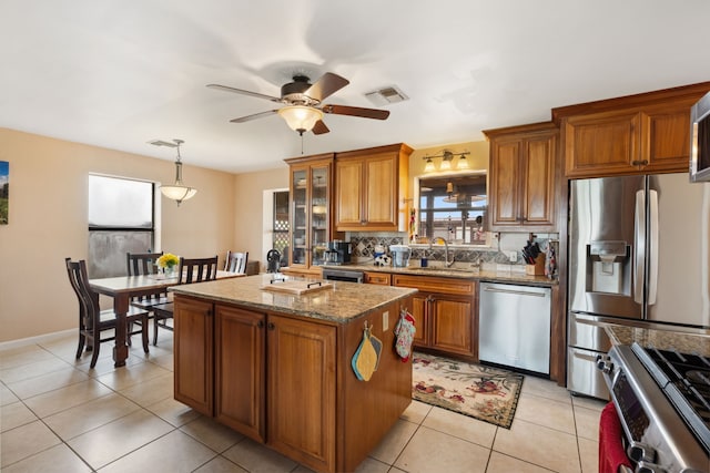 kitchen featuring visible vents, brown cabinetry, a kitchen island, a sink, and stainless steel appliances