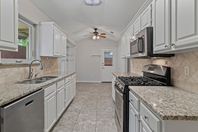 kitchen featuring a ceiling fan, appliances with stainless steel finishes, a sink, lofted ceiling, and white cabinetry