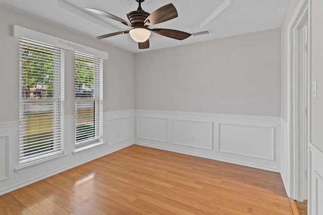 unfurnished room featuring a ceiling fan, wainscoting, light wood finished floors, and visible vents