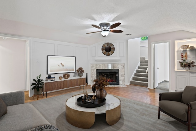 living area with ceiling fan, a textured ceiling, a fireplace, wood finished floors, and stairway