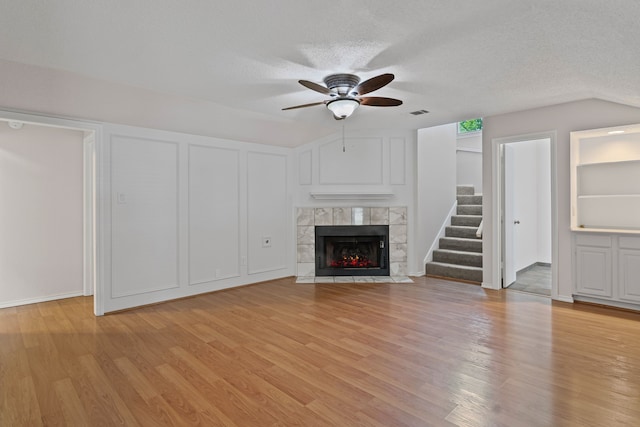 unfurnished living room with ceiling fan, a fireplace, a textured ceiling, light wood-style flooring, and stairs