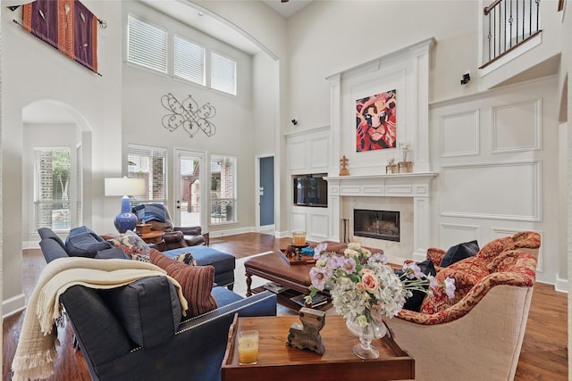 living room with a towering ceiling, arched walkways, baseboards, wood finished floors, and a high end fireplace