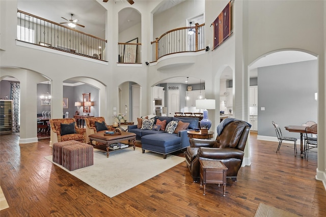 living area featuring baseboards, a high ceiling, a ceiling fan, and dark wood-style flooring
