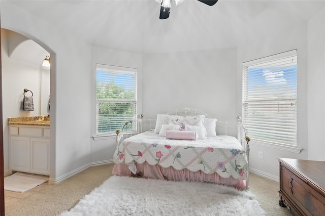 bedroom featuring a ceiling fan, light colored carpet, arched walkways, baseboards, and connected bathroom