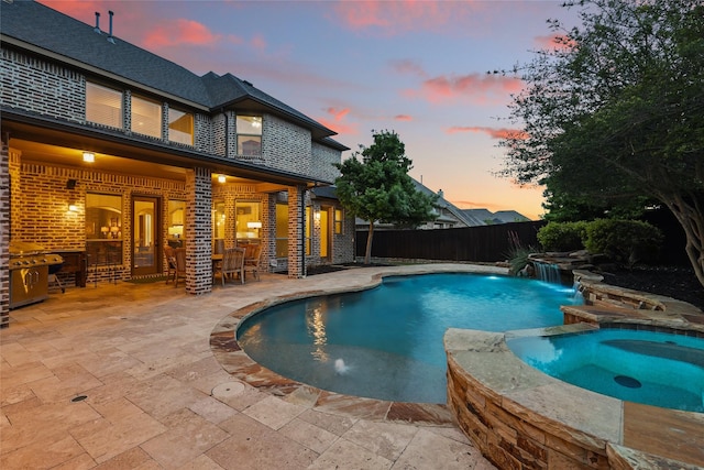 pool at dusk with a fenced backyard, outdoor dry bar, a patio, and a pool with connected hot tub