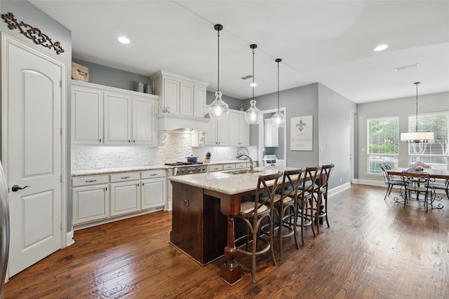 kitchen featuring a sink, decorative backsplash, a kitchen island with sink, and dark wood-style flooring
