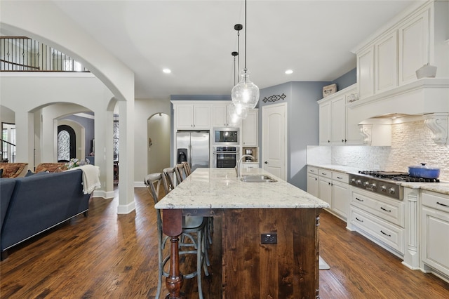 kitchen featuring a sink, arched walkways, a kitchen breakfast bar, stainless steel appliances, and backsplash