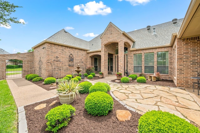 view of front of home featuring roof with shingles, a gate, a patio area, and brick siding