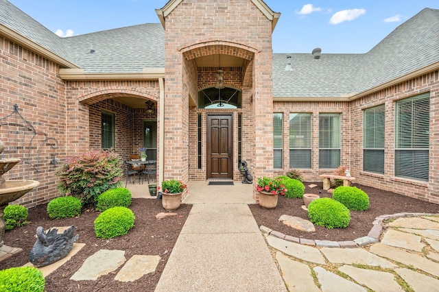 entrance to property featuring brick siding and roof with shingles