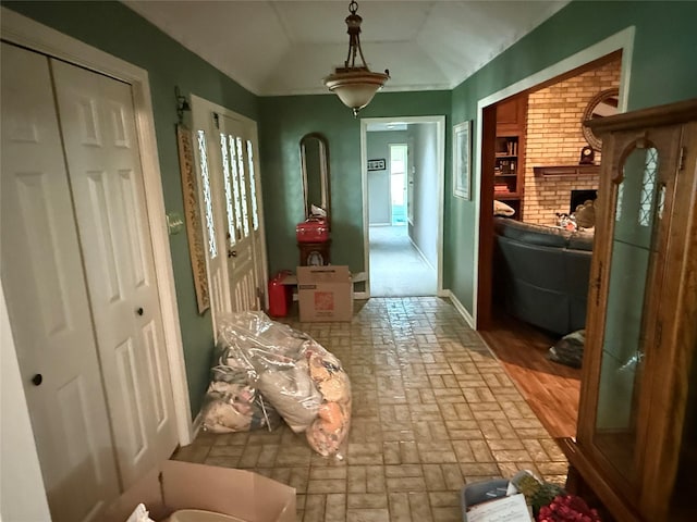 hall featuring baseboards, lofted ceiling, and brick floor