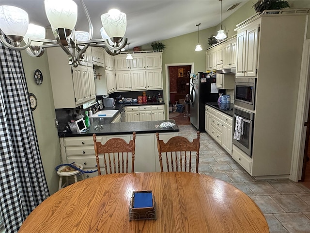kitchen with dark countertops, an inviting chandelier, stainless steel appliances, a peninsula, and under cabinet range hood