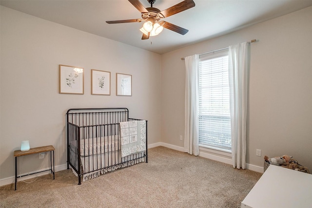 carpeted bedroom featuring a nursery area, baseboards, and ceiling fan