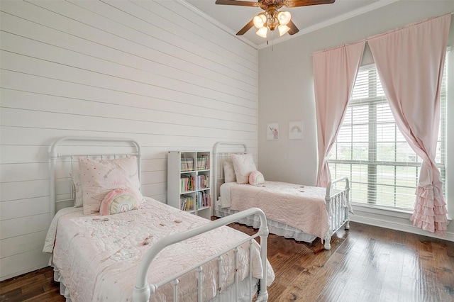 bedroom with wood-type flooring, wooden walls, a ceiling fan, and ornamental molding