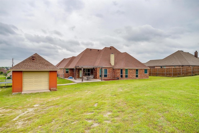 rear view of property featuring fence, an outbuilding, a patio area, a yard, and a detached garage