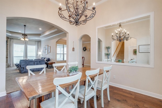 dining space with crown molding, wood finished floors, baseboards, a tray ceiling, and arched walkways