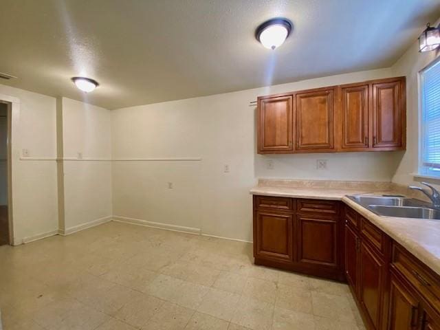 kitchen featuring brown cabinetry, a sink, baseboards, and light countertops