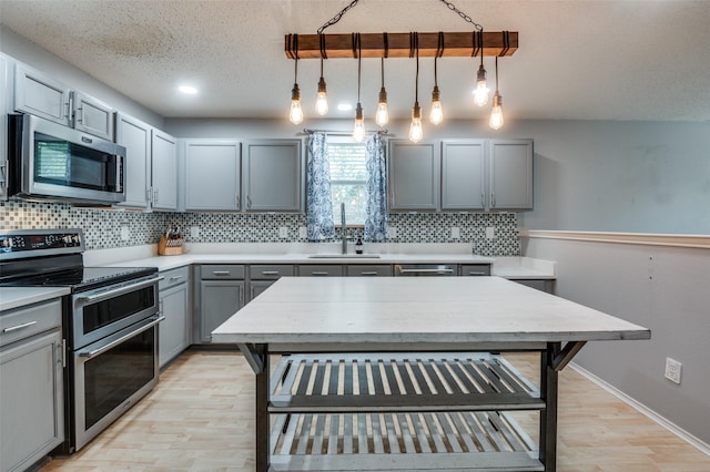 kitchen with light wood-style floors, tasteful backsplash, a sink, appliances with stainless steel finishes, and gray cabinetry