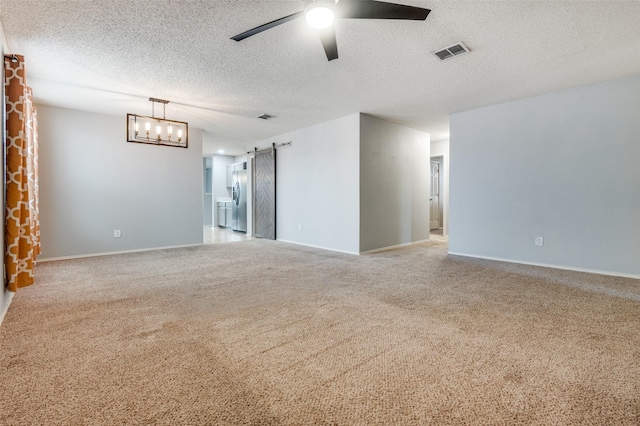 carpeted spare room featuring a textured ceiling, visible vents, a barn door, baseboards, and ceiling fan with notable chandelier