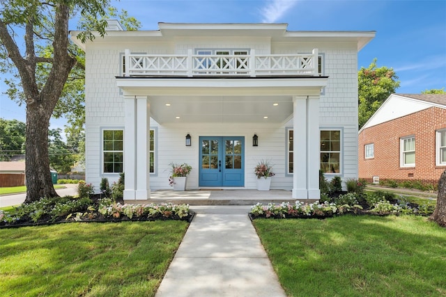 view of front of home with french doors, covered porch, a front yard, and a balcony