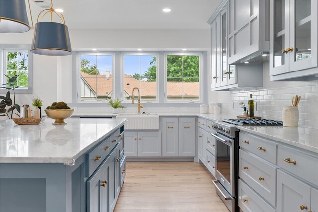kitchen featuring decorative backsplash, light stone countertops, high end range, a sink, and light wood finished floors
