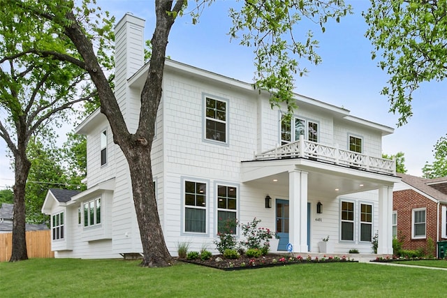 view of front of home with fence, a chimney, a front lawn, and a balcony