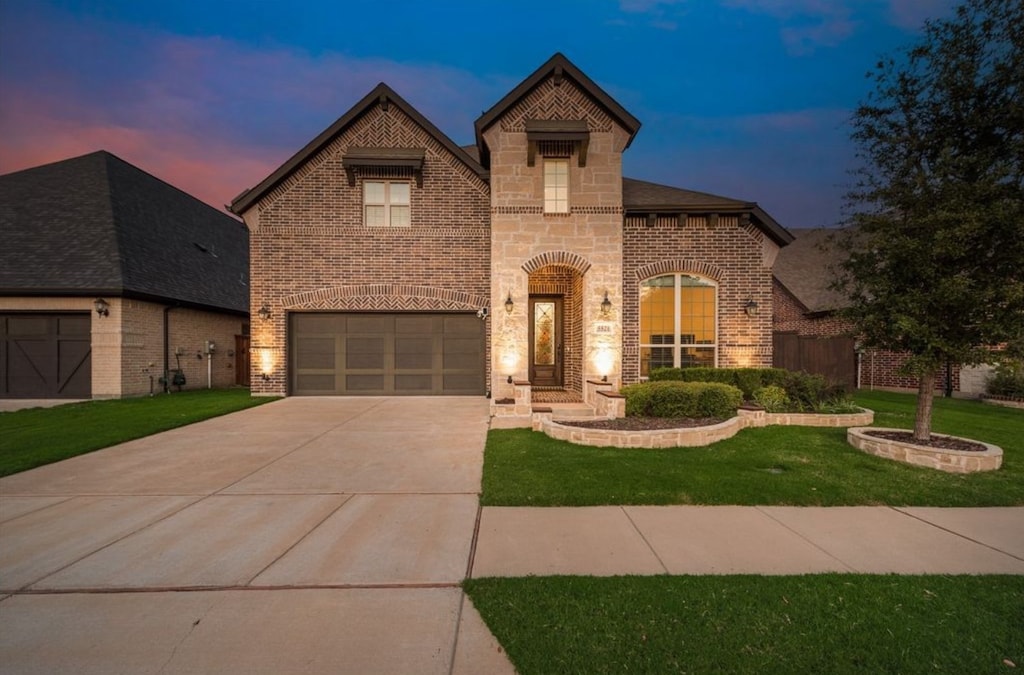 view of front of home featuring driveway, brick siding, a yard, an attached garage, and stone siding