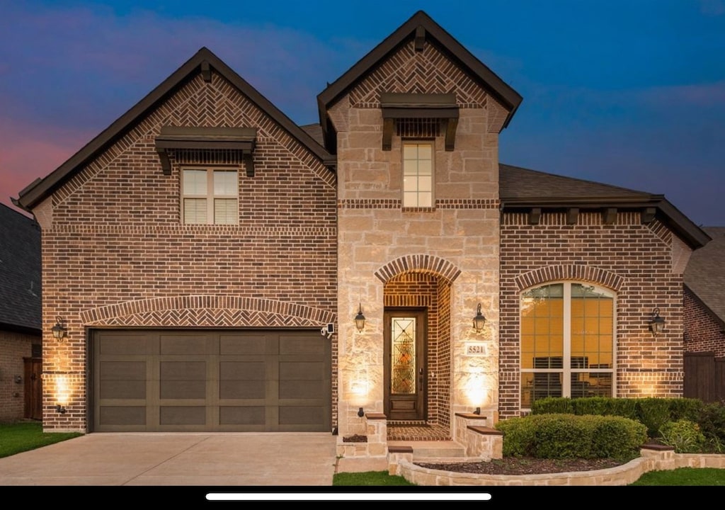 french country home with an attached garage, concrete driveway, stone siding, and brick siding