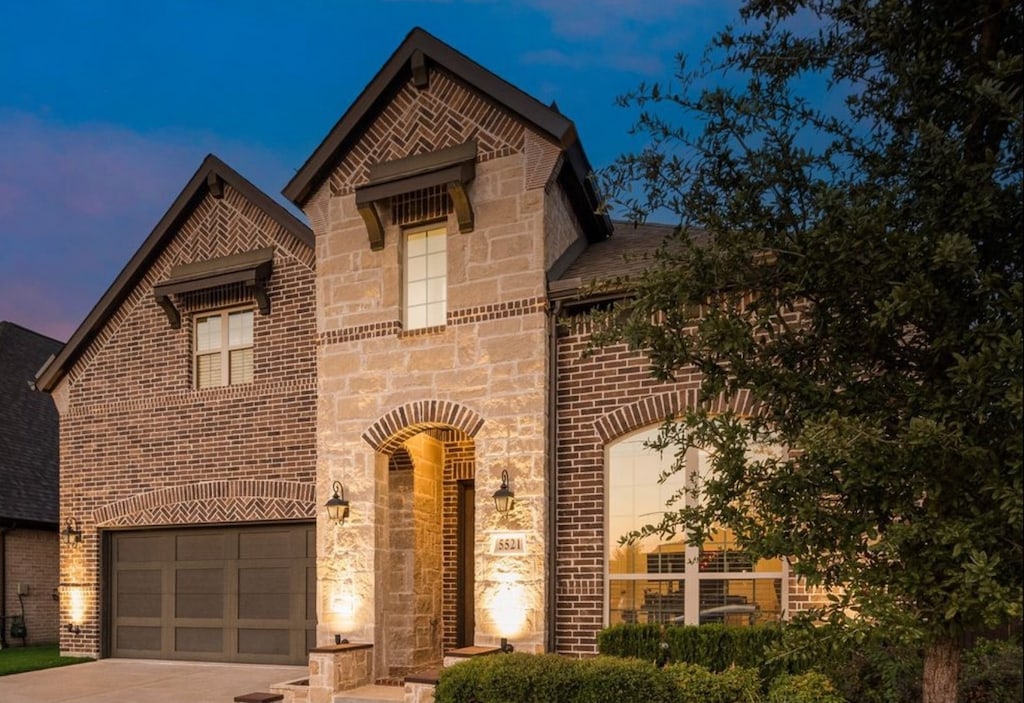 view of front of property featuring brick siding, an attached garage, driveway, and stone siding