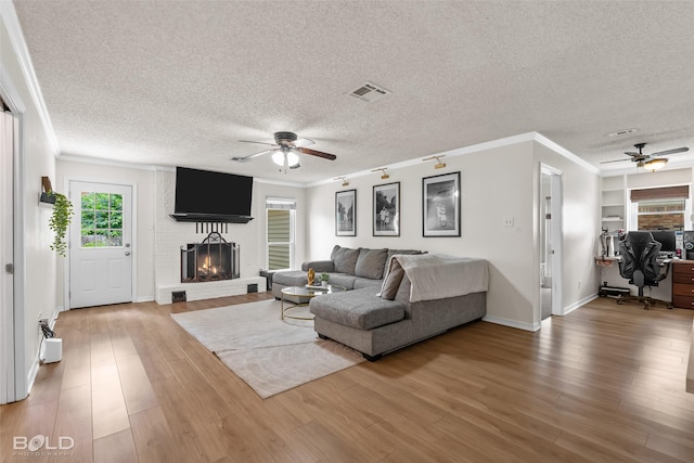 living room with crown molding, a fireplace, a textured ceiling, a ceiling fan, and visible vents