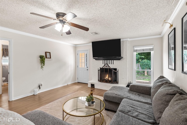 living room with a fireplace, a textured ceiling, a healthy amount of sunlight, wood finished floors, and visible vents