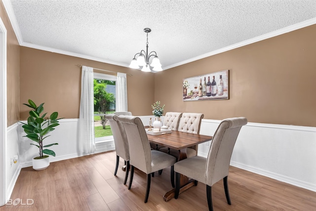 dining space with a textured ceiling, a notable chandelier, ornamental molding, and wood finished floors