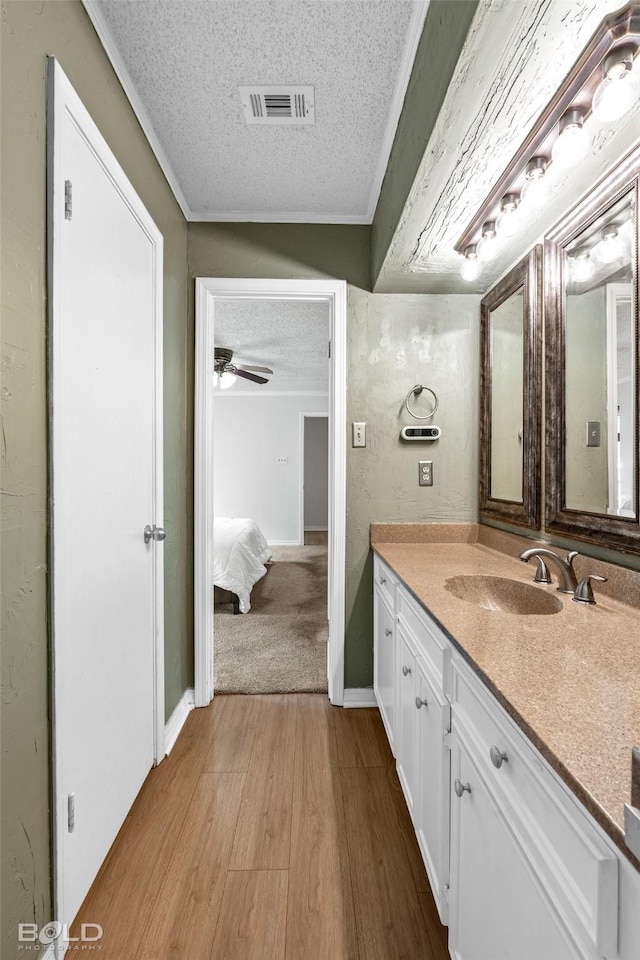 bathroom with vanity, a textured ceiling, wood finished floors, visible vents, and ornamental molding